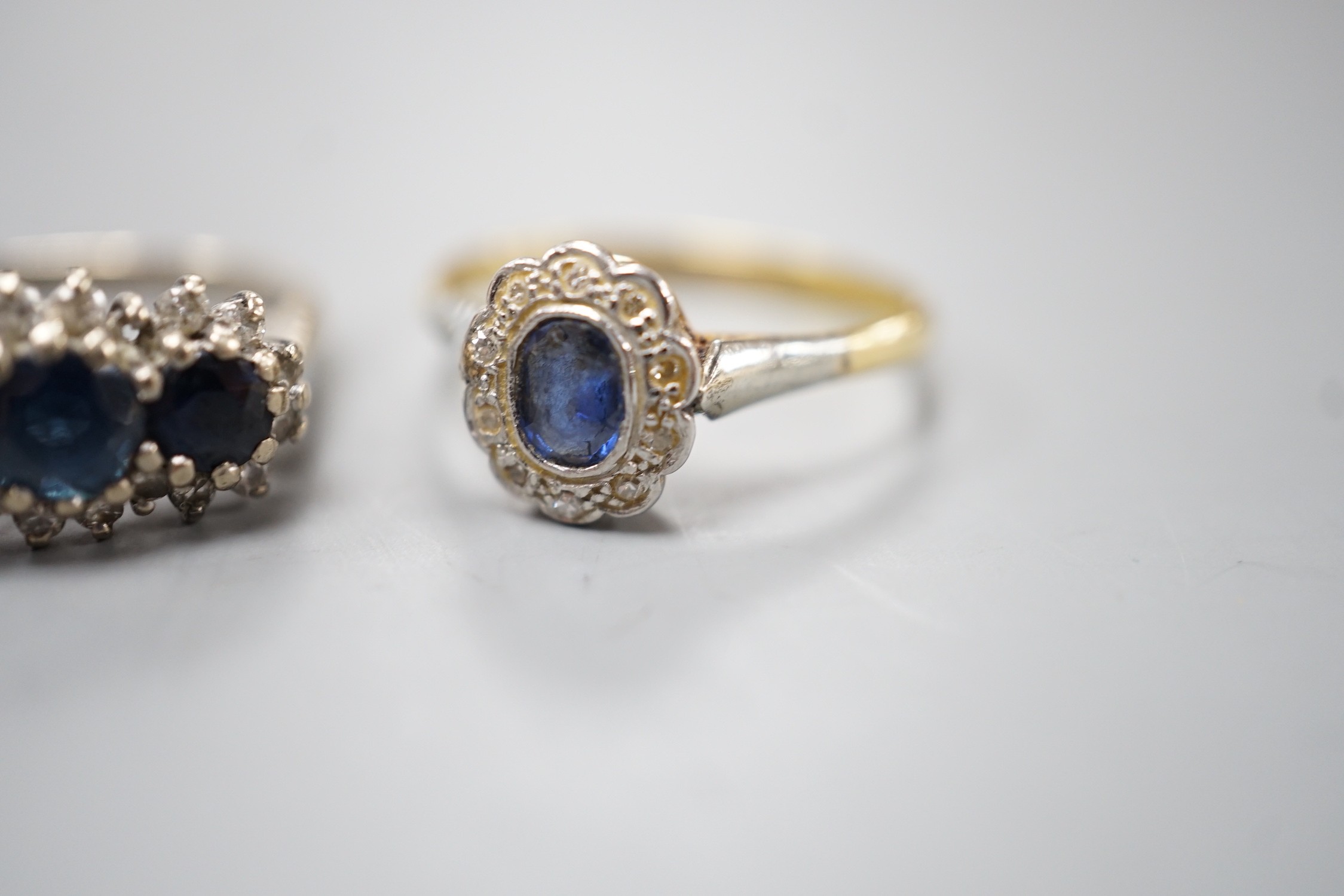 An 18ct white metal, sapphire and diamond set triple cluster ring, size O and a yellow metal, sapphire and diamond set oval cluster ring, size O/P, gross weight 6.8 grams.
